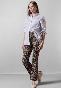 Bílá košile na knoflíky, kalhoty s vysokým pasem s leopardím potiskem a béžové tenisky. Hladká látka s výrazným vzorem zvířat; volný střih.