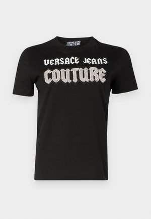 Black cotton t-shirt featuring "VERSACE JEANS COUTURE" in bold, white, textured lettering and jeweled detailing across the chest. Short sleeves.
