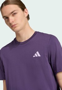 Paarse katoenen t-shirt met een ronde halslijn en korte mouwen. Heeft een lichtpaarse Adidas-logo op de linkerborst. Soepele textuur.