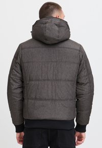 Padded gray jacket with a hood, featuring a textured fabric, ribbed cuffs, and horizontal stitching. The back view shows a relaxed fit.
