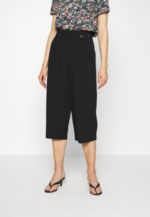Pantaloni culotte neri con un design sartoriale, caratterizzati da tasche laterali e doppi bottoni decorativi in vita. Tessuto dalla texture liscia.