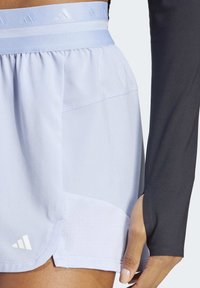 Light blue athletic skirt features a gathered waistband, side mesh panel, and folded hem detail, accented with the Adidas logo in white.