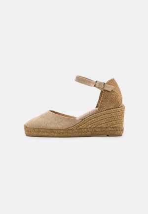 Espadrille compensée beige avec bout fermé, bride à la cheville avec boucle et semelle plateforme en jute tressée.