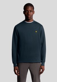 Marinblå långärmad sweatshirt med rund halsringning, prydd med en liten gul broderad logotyp på vänster bröst och ribbade muddar.