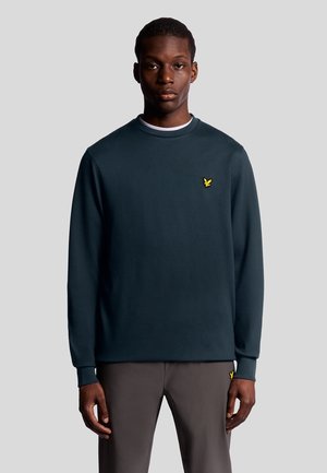 Sweatshirt à manches longues bleu marine avec un col rond, arborant un petit logo jaune brodé sur la poitrine gauche et des poignets côtelés.