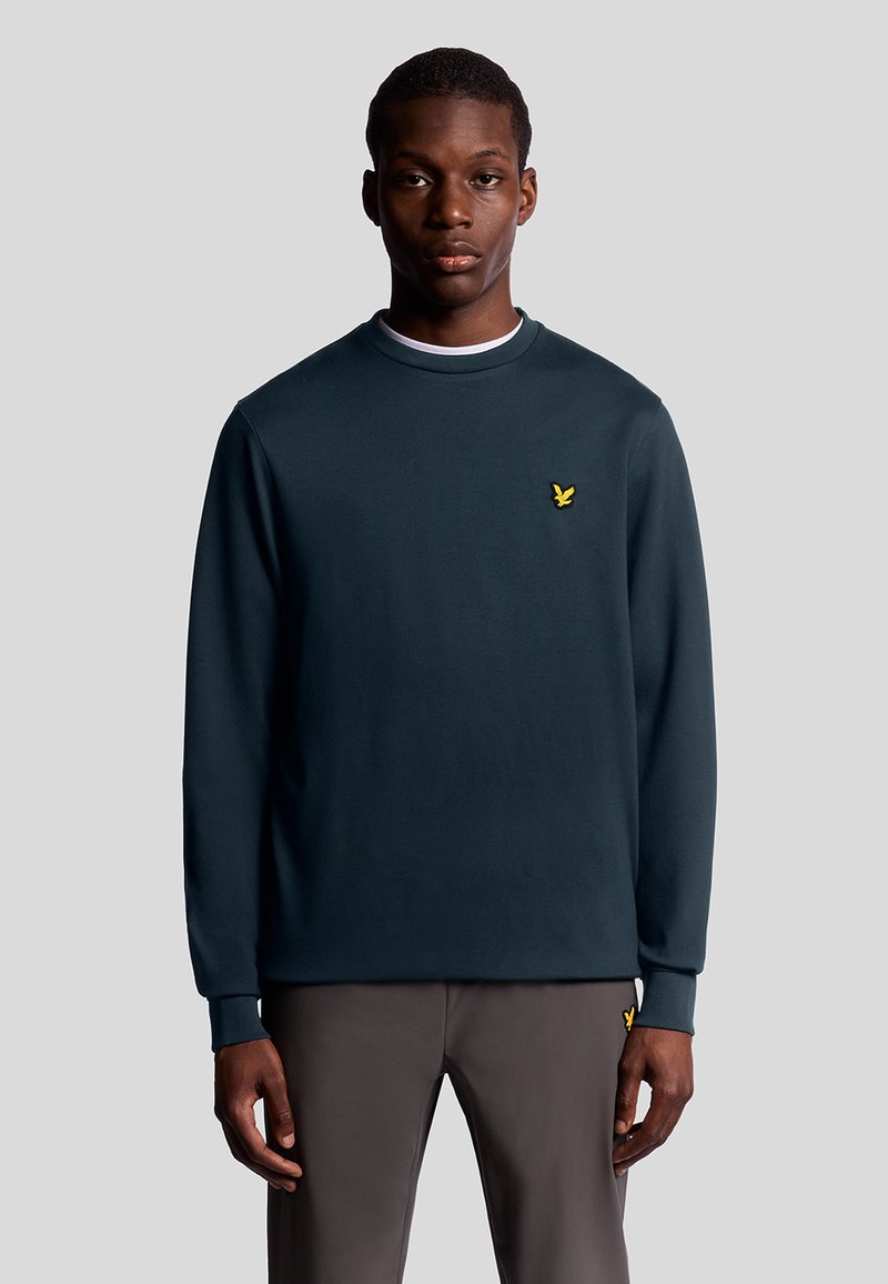 Marinblå långärmad sweatshirt med rund halsringning, prydd med en liten gul broderad logotyp på vänster bröst och ribbade muddar.