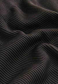 Schwarzer gerippter Stoff mit wellenförmiger Textur, ausgeprägten horizontalen Linien und einem weichen, dehnbaren Aussehen.