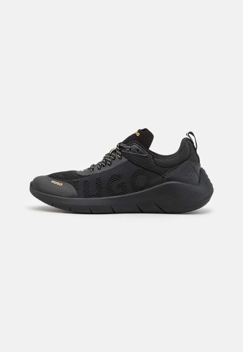 Baskets de sport noires avec empeigne en mesh, lacets à motifs et semelle épaisse, marquées de "Hugo" en lettres dorées sur le côté et la languette.