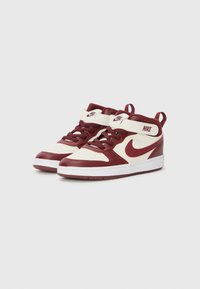 Vínové a krémové vysoké tenisky s bielymi podrážkami a logom Nike, umiestnené vedľa seba na jednoduchom pozadí.