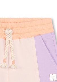 Joggers légers présentant une palette de couleurs pastel de pêche, crème et lavande. Taille élastique avec un cordon de serrage décoratif et une étiquette de logo.