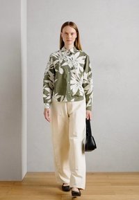 Chemise à boutons verte à motif floral avec des manches longues, associée à un pantalon large crème et un sac à main noir. Tissu lisse et décontracté.