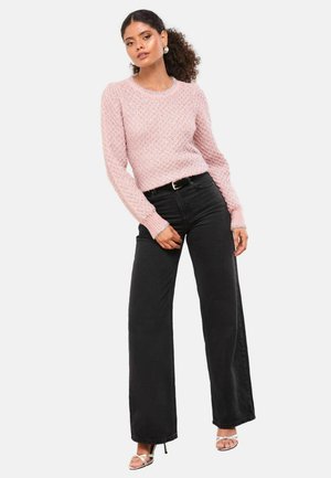 Rozā adīta džemperis ar teksturētu dimanta rakstu, apvienots ar augsto vidukli melnām platiem biksēm. Modelis valkā sudraba papēžu sandales.