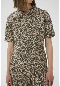 Leopard-print jumpsuit in beige and olive, short sleeves, front zip closure, and two chest pockets with a fitted waist.