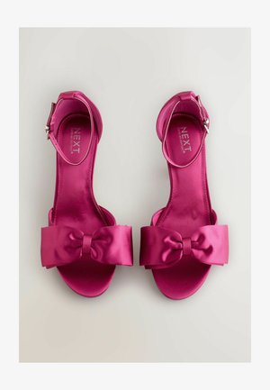 Fuchsiové saténové sandále s širokou mašľou, otvorenou špičkou a nastaviteľným popruhom okolo členka. Hladká textura a plochý dizajn podrážky.