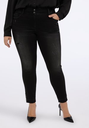 Jeans skinny neri con un leggero effetto usato, chiusura a due bottoni e una texture elegante. Presentano accessori decorativi alla caviglia.