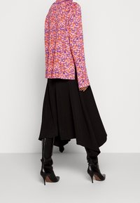 Långärmad topp i lila, rosa och orange blommönster, kombinerad med en fladdrande svart kjol och knähöga svarta klackstövlar.