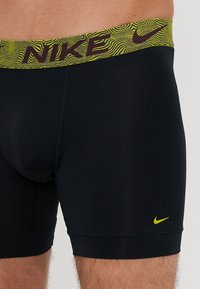 Fekete Nike boxer alsónadrág sárga, mintás derékrésszel, amelyen a márka logója található. Simább anyag, testhezálló fazon és rövid hosszúság jellemzi.