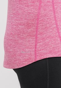 Rosa melierte Sportshirt mit kurzen Ärmeln, gebogenem Saum und einem "DRI-FIT"-Label nahe dem unteren Rand. Darunter getragen mit schwarzen Leggings.