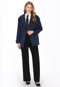 Tengerészkék dupla soros gombolású ballonkabát nagy gombokkal, vállpántokkal és laza szabással, fekete nadrággal és fehér inggel párosítva.