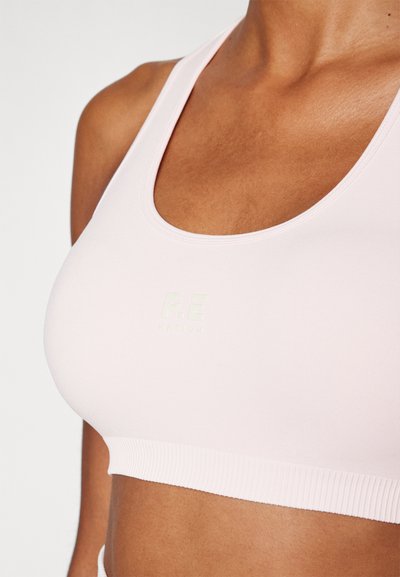 Sutiã desportivo rosa claro feito de um tecido suave e elástico. Apresenta uma faixa inferior canelada e um logotipo discreto na frente.