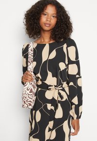 Vestido padrão preto e castanho com mangas longas e cinto na cintura, combinado com uma bolsa de padrão abstrato castanho e branco. Textura de tecido suave.