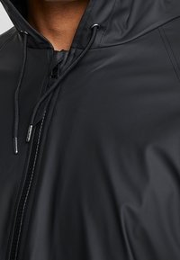 Czarna wodoodporna kurtka z zapięciem na zamek błyskawiczny, kapturem ze ściągaczem i gładką fakturą. Wyróżnia się minimalistycznym designem i eleganckim wykończeniem.