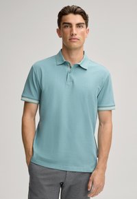 Polo bleu clair en tissu texturé, avec un col et des ourlets de manches rayés contrastants. Logo discret sur le devant. Manches courtes, coupe décontractée.