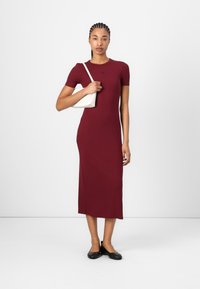 Burgundy ribbed midi dress with short sleeves, paired with a white shoulder bag and black flats. Simple, body-hugging silhouette.