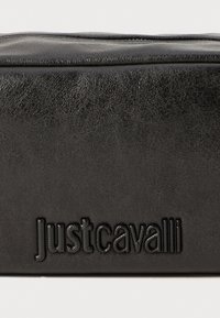 Fekete műbőr táska, amelyen a "Justcavalli" logó domborúan megjelenik, téglalap alakú, sima textúrával, finom ráncokkal a részletekért.