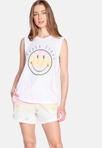 Witte mouwloze shirt met een smiley-gezicht graphic en de tekst "Happy Vibes." Gepaard met lichtgekleurde shorts met smiley-motieven.
