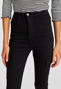 Pantalones cargo negros de tiro alto hechos de denim, con bolsillos delanteros, un botón de metal y un sutil detalle de costura en los lados.