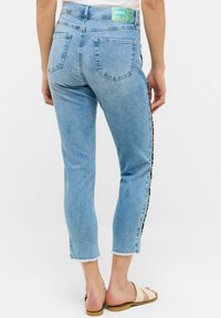 Svetlomodré džíny z denimu s crop strihom, roztrhnutým lemom a bočným akcentovým vzorom. Obsahujú dve zadné vrecká a označenie pásu značky.