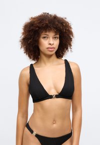 Μαύρο σετ μπικίνι με ριγωτή υφή, βαθύ ντεκολτέ και ρυθμιζόμενες τιράντες. Το τοπ διαθέτει χρυσό κούμπωμα μπροστά.