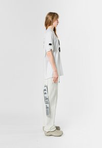 Camiseta blanca de gran tamaño con texto gráfico negro, combinada con pantalones anchos de color claro que presentan un diseño impreso y detalles de bolsillos de utilidad.