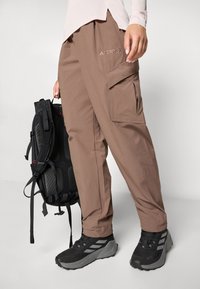 Brown cargo pants with side pockets, branded "TERREX." Paired with black athletic shoes and a black backpack featuring adjustable straps.