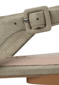 Gros plan sur une bride de sandale en daim beige avec une boucle carrée et une semelle intérieure marron lisse.