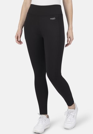 Schwarze Leggings mit hohem Bund, aus dehnbarem Material gefertigt, mit einem Logo an der Hüfte und einer glatten Textur. Getragen mit weißen Sneakers.
