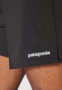 Black Patagonia shorts made of smooth fabric, featuring a white logo on the hem. The design is simple with clean stitching details.