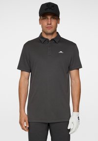 Grå polo skjorta med krage och korta ärmar. Har en liten vit logotyp på bröstet. En matchande grå keps fulländar outfiten.