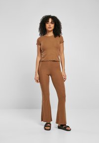 Ensemble deux pièces marron à côtes comprenant un haut à manches courtes avec des bords festonnés et un pantalon évasé. Les sandales sont noires avec une semelle plate.