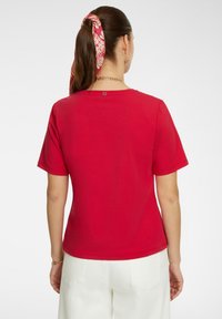 T-shirt rossa a maniche corte con scollo rotondo, texture liscia e un piccolo dettaglio del logo sul retro vicino allo scollo.