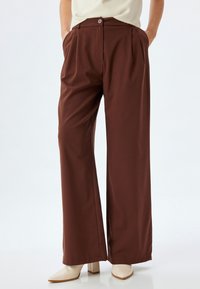 Brown wide-leg trousers with a high waist, featuring a single button closure, front pleats, and soft, smooth fabric texture.