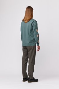 Majica z dolgimi rokavi v teal barvi s teksturiranimi vzorci listov na rokavih, v kombinaciji z olivnimi hlačami in črnimi čevlji, gledano s hrbtne strani.