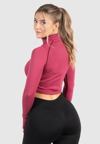 Bordový zkrácený rolák s dlouhými rukávy, ribbovaná textura, kontrastní švy, ve spojení s černými legínami. Na neutrálním pozadí.