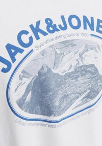 Hvid bomuld t-shirt med blåt grafisk tryk af bjerge og mærkenavnet "JACK & JONES," med rund kontur og tekst i forskellige skrifttyper.