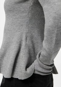 Pull en maille côtelée gris avec des poignets côtelés, associé à un pantalon noir, montrant des détails sur les côtés et les bras dans un tissu doux.