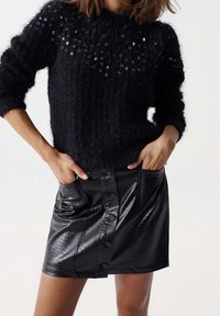 Černý pletený svetr se zdobením z flitrů, kombinovaný s lesklou černou mini sukni z umělé kůže s knoflíkovými detaily a bočními kapsami.