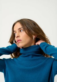 Tiefblaues Rollkragensweater aus weichem Strickstoff, mit einem gerippten Kragen und glatter Textur, vor einem neutralen Hintergrund getragen.