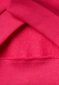 Tessuto rosa brillante con una superficie liscia e texture e dettagli a costine. Presenta sezioni sovrapposte con cuciture uniformi e un colore consistente.
