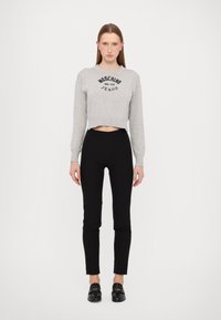 Pelēks īss sporta krekls ar melnu tekstu "Moschino Jeans", apvienots ar melnām piegulošām biksēm un melniem slip-on apaviem.